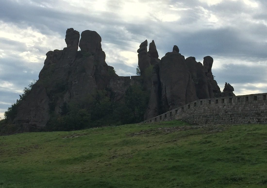 imposing rock formations above a medieval wall and green field