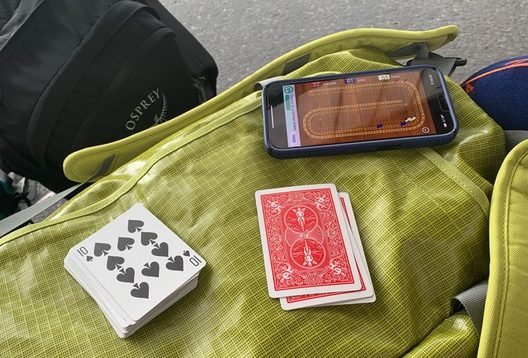 cards and phone on a cribbage board app lying on a stack of backpacks