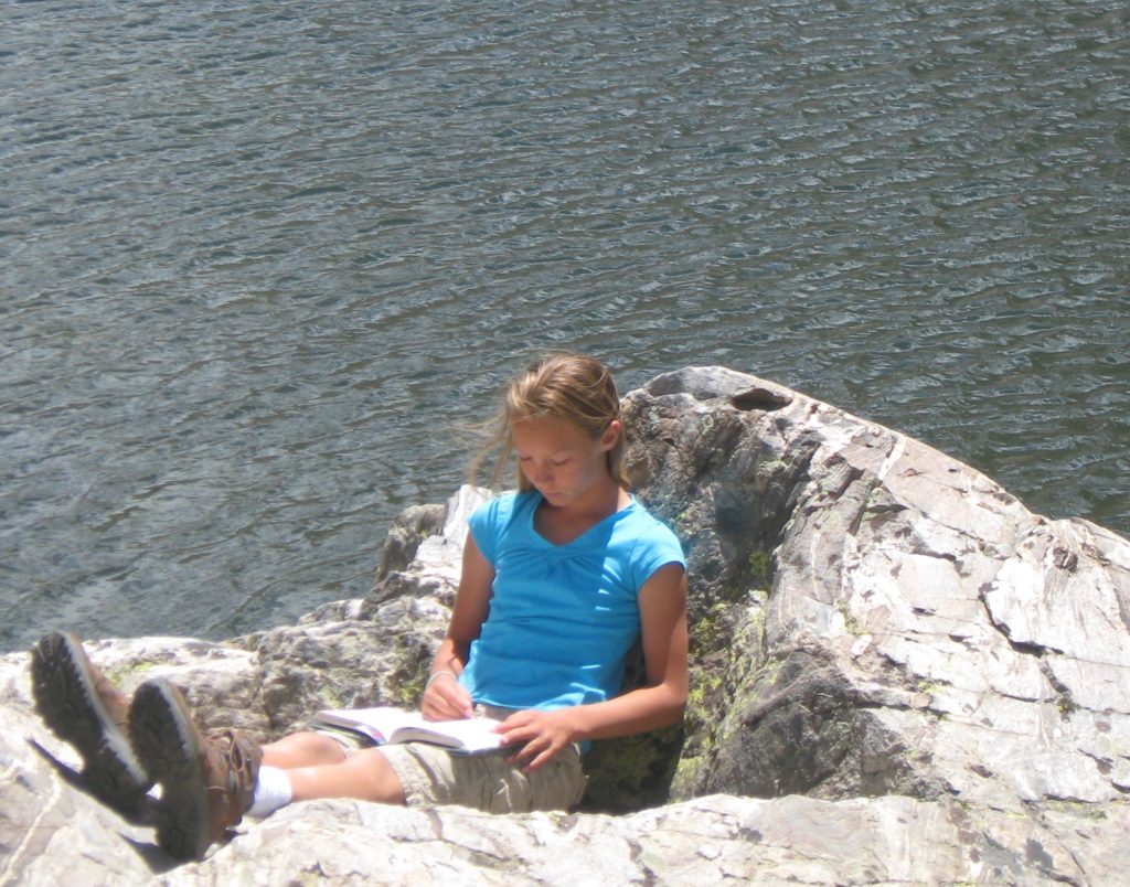 Young Maddie reading on a rock by a lake