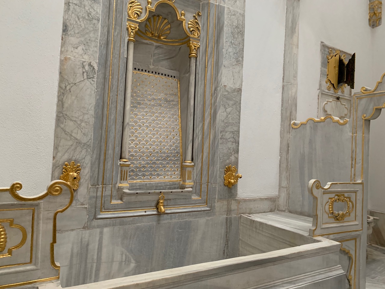 A marble and gold alcove with a faucet and rectangular bathing pool