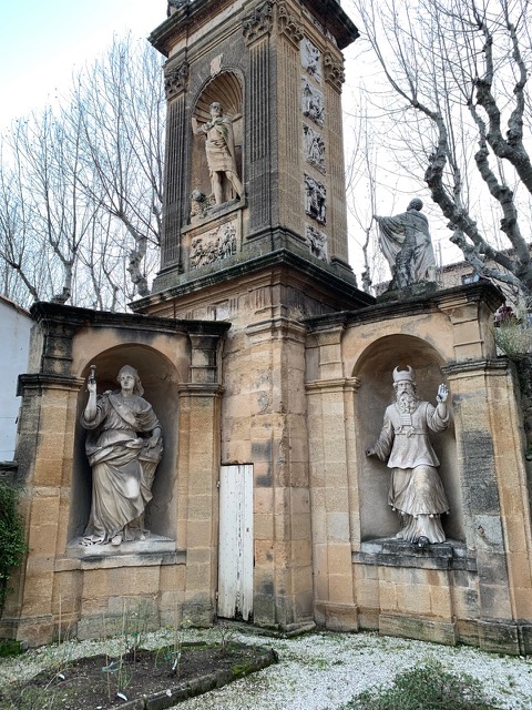 Two white statues tucked into alcoves in a garden