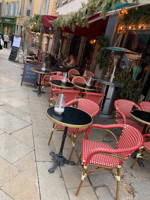 red and white wicker chairs around round tables in front of a restaurant with a lot of plants
