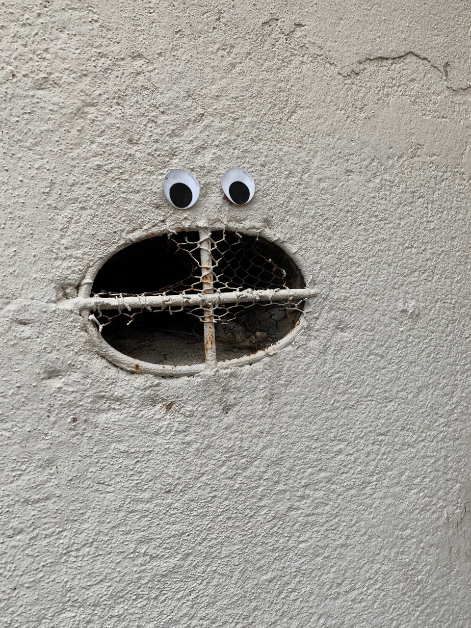 A holy in a wall with two googly eyes placed above