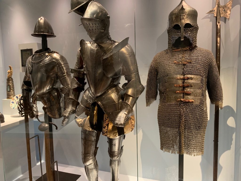 Three stands of metal armor in three different medieval styles