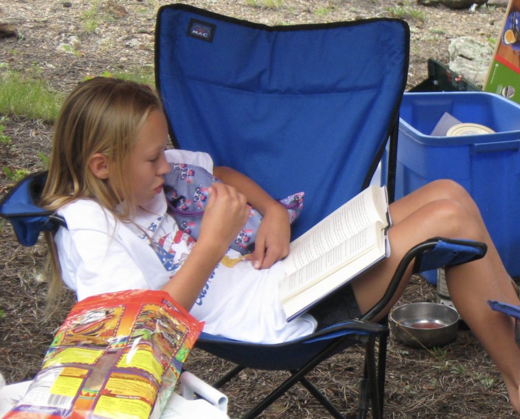 Young Maddie reading in a camp chair
