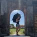 Maddie standing sideways with an umbrella over her shoulder framed by the curved archway of a wall in the old imperial palace of Hue